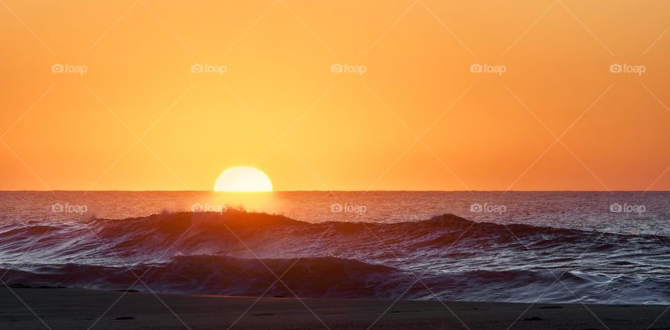 The sunsets behind the crashing waves of the Atlantic Ocean on the beach at Paredes da Vitória, Portugal 