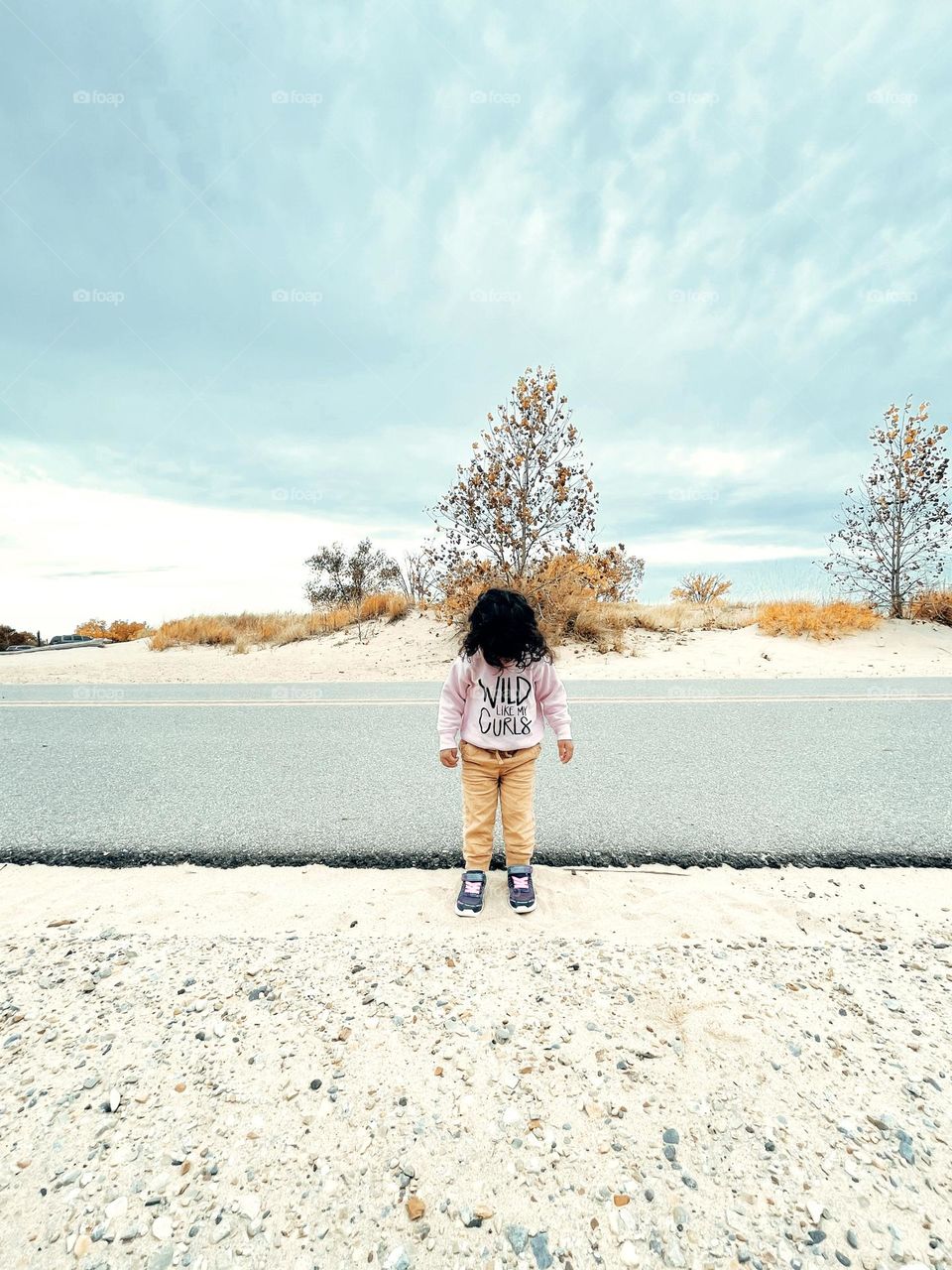 Wild like my curls, little girl with curly hair standing by the road, hair as an accessory, wild curly hair on toddler girl, toddler with crazy hair, toddler looking down on beach road 