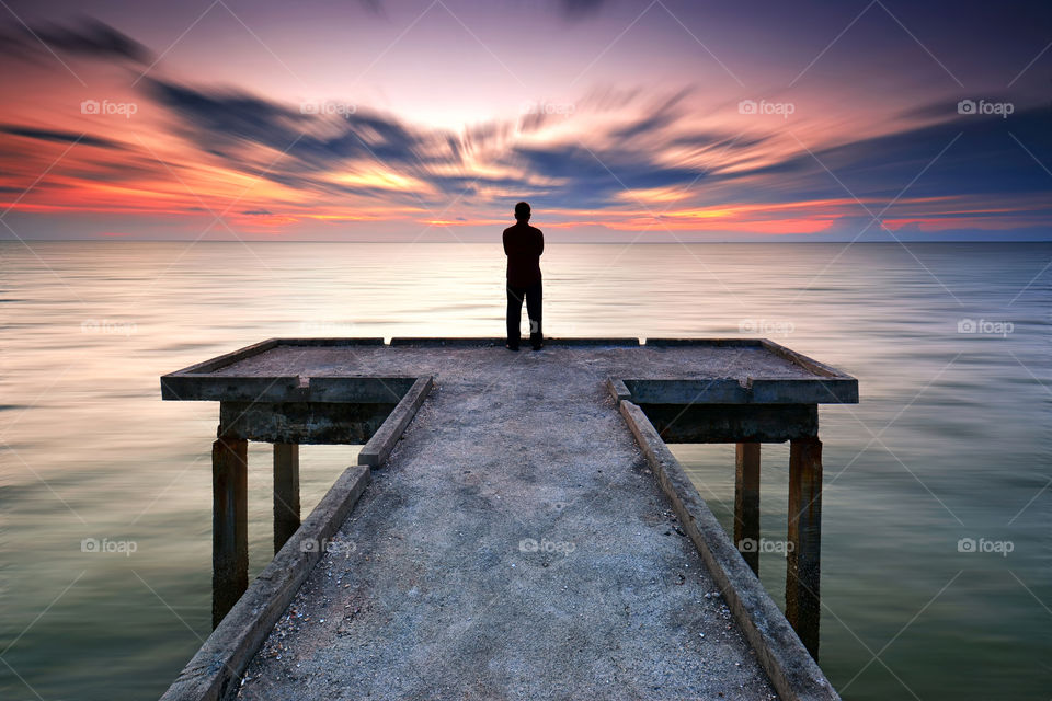 A man standing on the pier facing beautiful seascape sunset