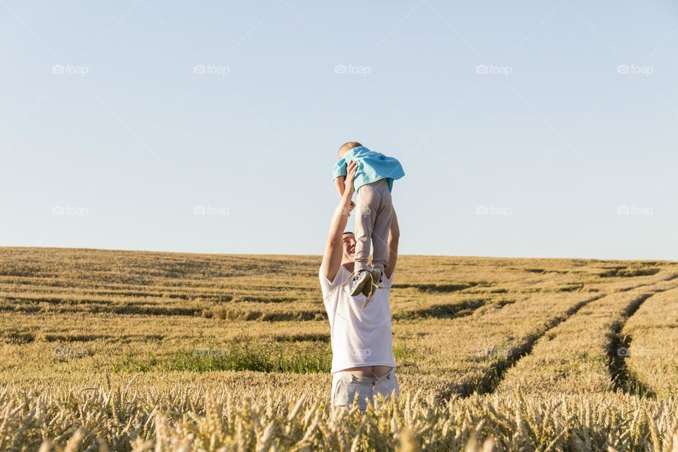 Dad and son are walking in a field with ripe wheat during the harvest.
