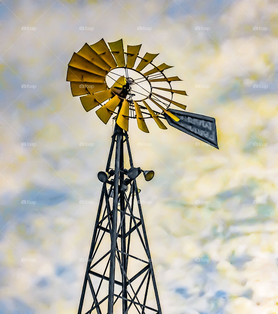 A tall vintage windmill standing tall against a beautiful backdrop of clouds on a windy day. 