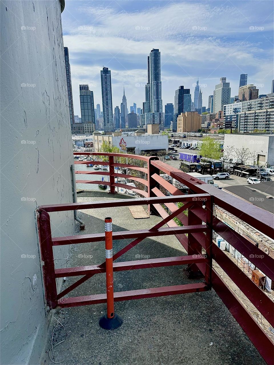 The orange red of the railings of the central outpost of the “Pulaski Bridge” that connects LIC, Queens to “Greenpoint”, Bklyn is juxtaposed to its complementary blue in the skyline of LIC and “Manhattan” and the sky above. 2025. Hypnotic Productions