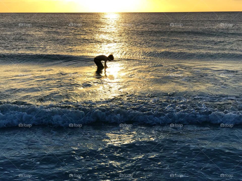 Small boy in the water during a golden ocean sunset.
