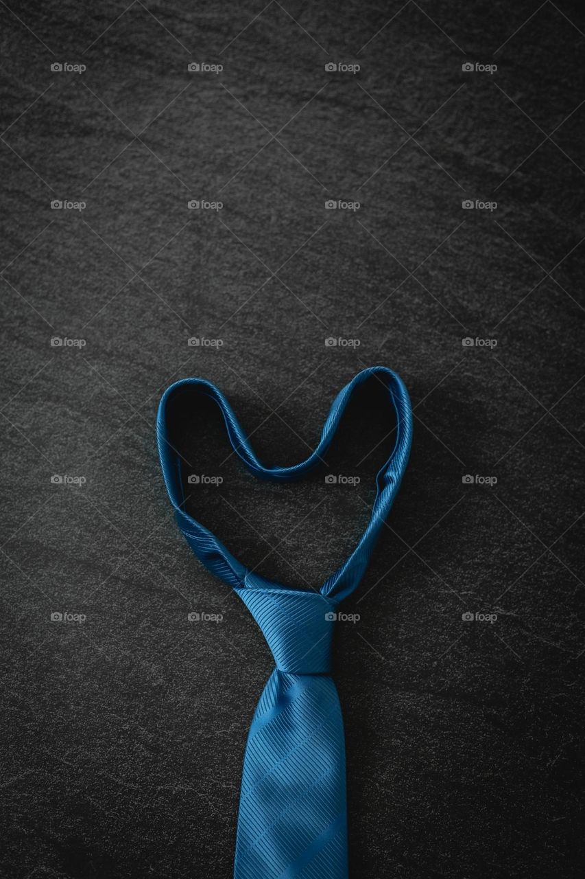 One blue heart-shaped tie lies in the center on a black stone background, flat lay close-up. Men's clothing concept.