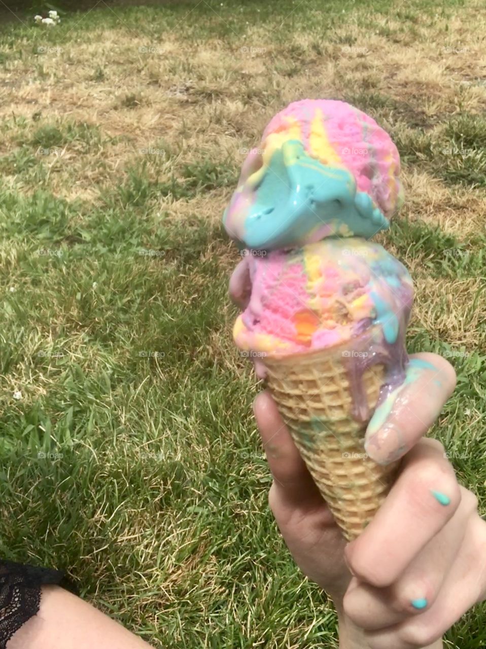 Holding a delicious rainbow colored ice cream and cone outdoors on a sunny day 
