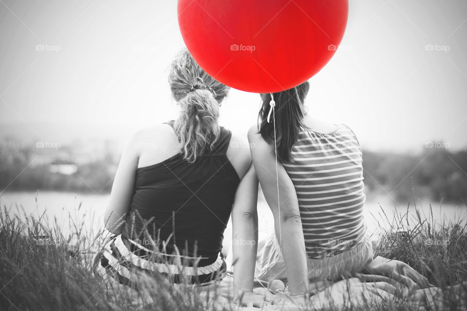 two girls with big red balloon. two girl friends sitting relaxing with big red ballon