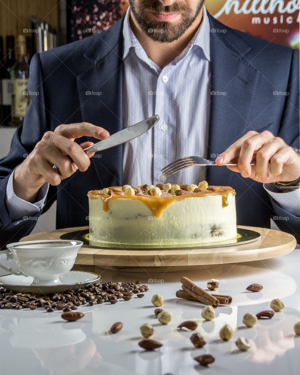 A man in a suit eats an entire cake with caramel topping with a knife and fork. Maybe it's his birthday today.
