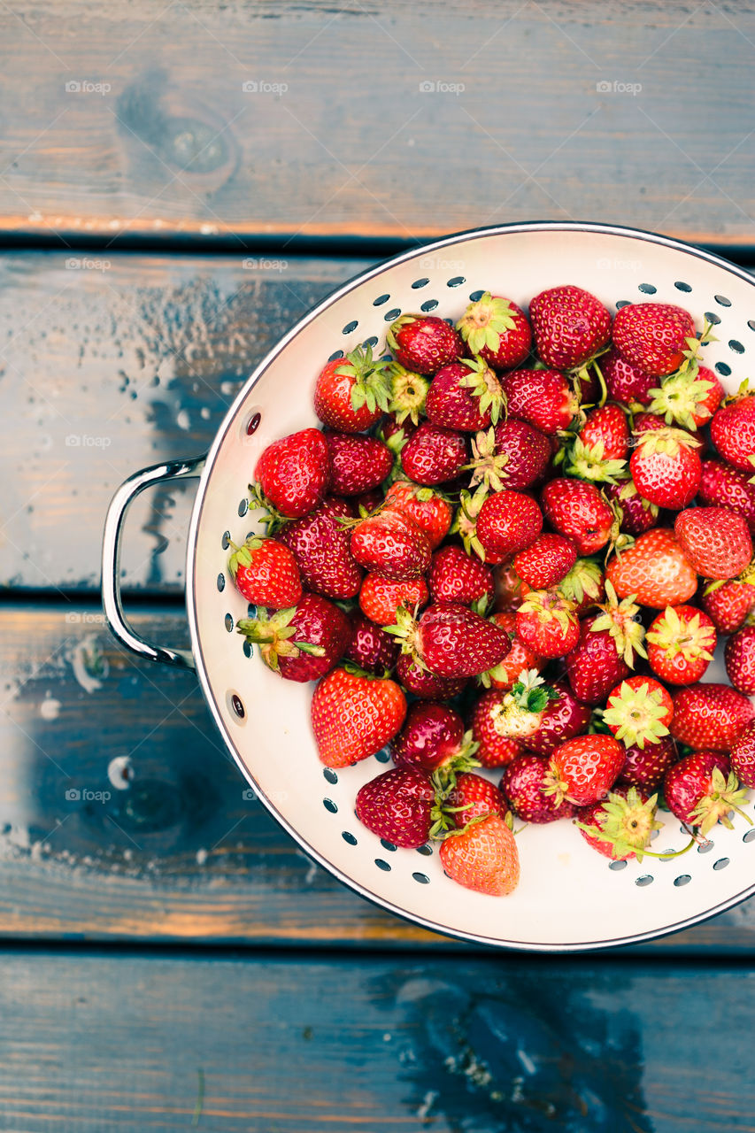 Closeup of bowl of fresh strawberries sprinkled raindrops on wooden table