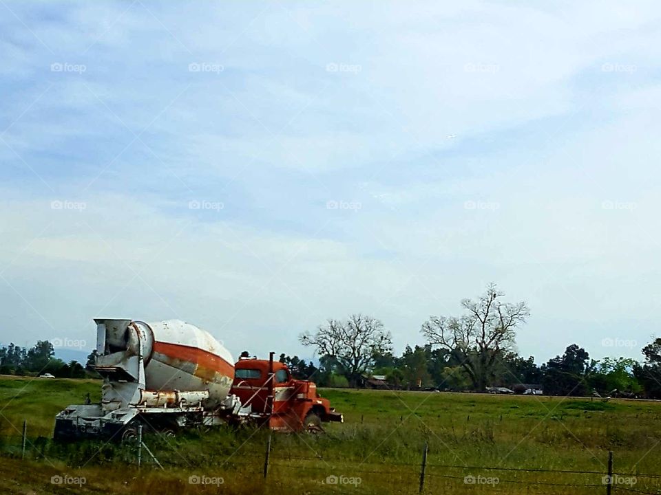 an abandoned cement mixer alone in a field ,going no where.