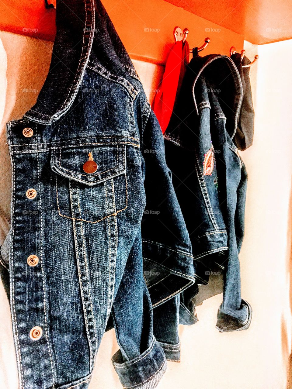 Pair of blue jeans jackets hanging close together on on a orange poles.