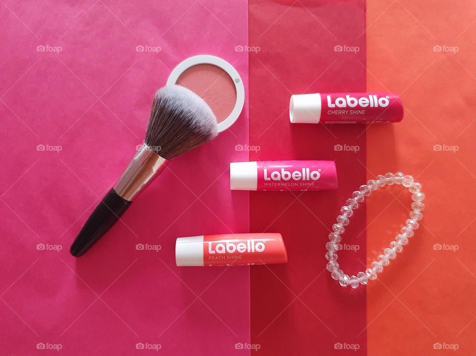 Labello Watermelon, cherry and peach shine flatlay on peach, cherry and watermelon paper surface with peach blush, blush brush and sparkling white crystal beads bracelet