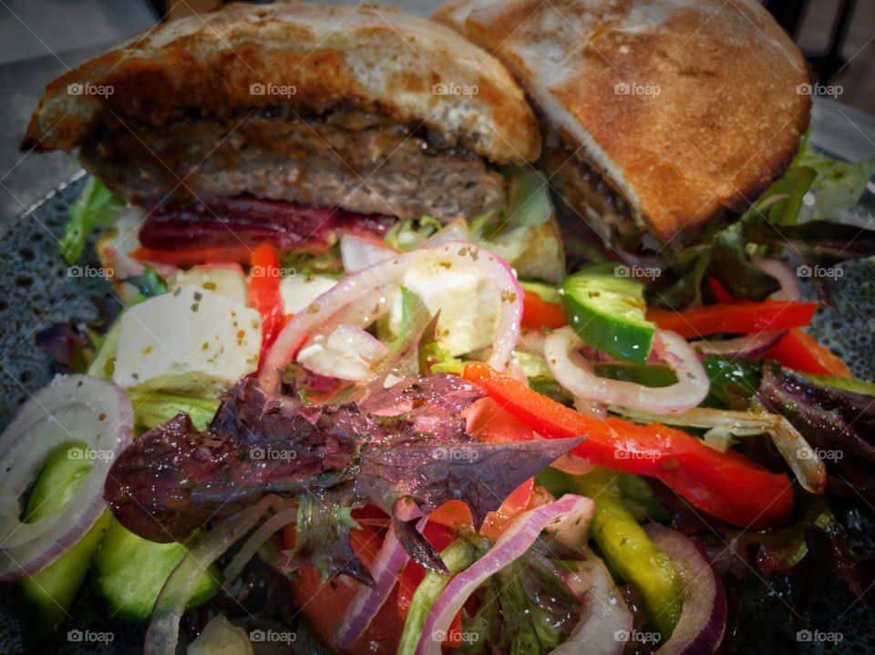 Hamburger on a serving plate that has been cut in halves. Close-up of colorful salad on side of the dish.