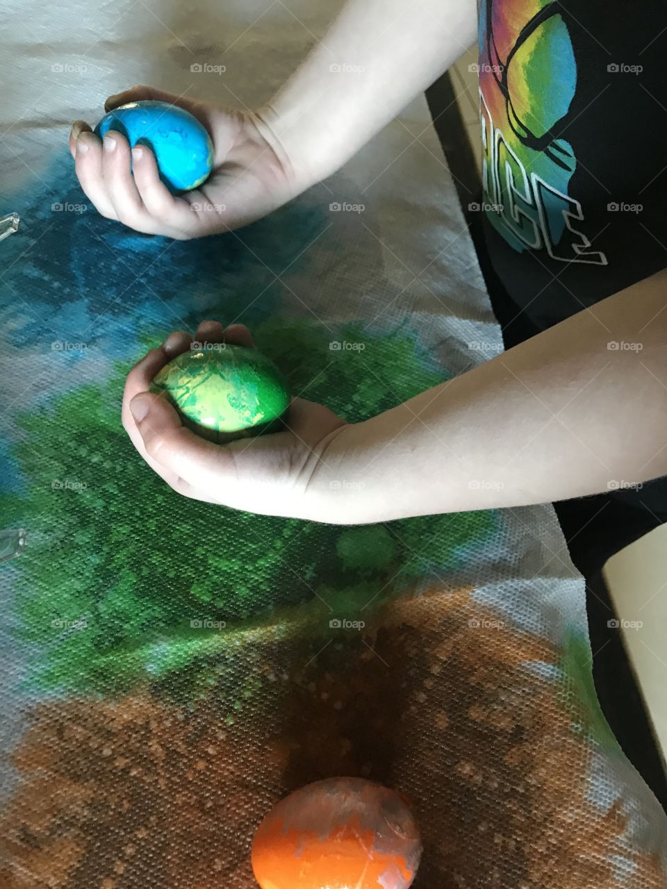 A child holding a green and blue colored Easter eggs in his hand 