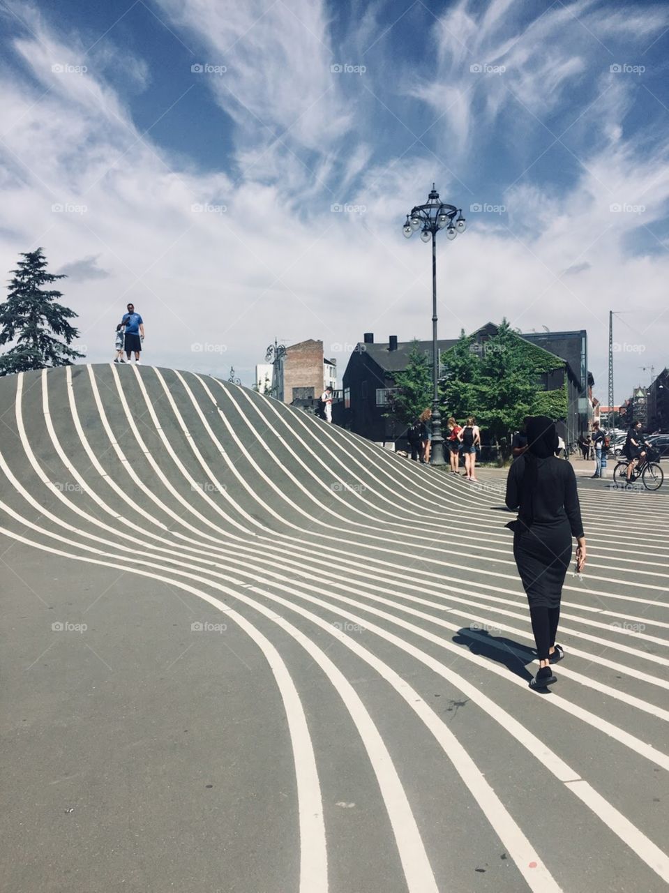 Urban park with black asphalt has crisp, symmetric, white lines leading up a hill. Art installations are on either side of the road. 