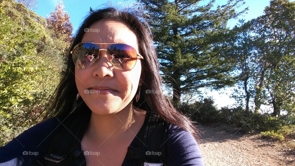 Asian woman with sunglasses close up photo while hiking outdoors.