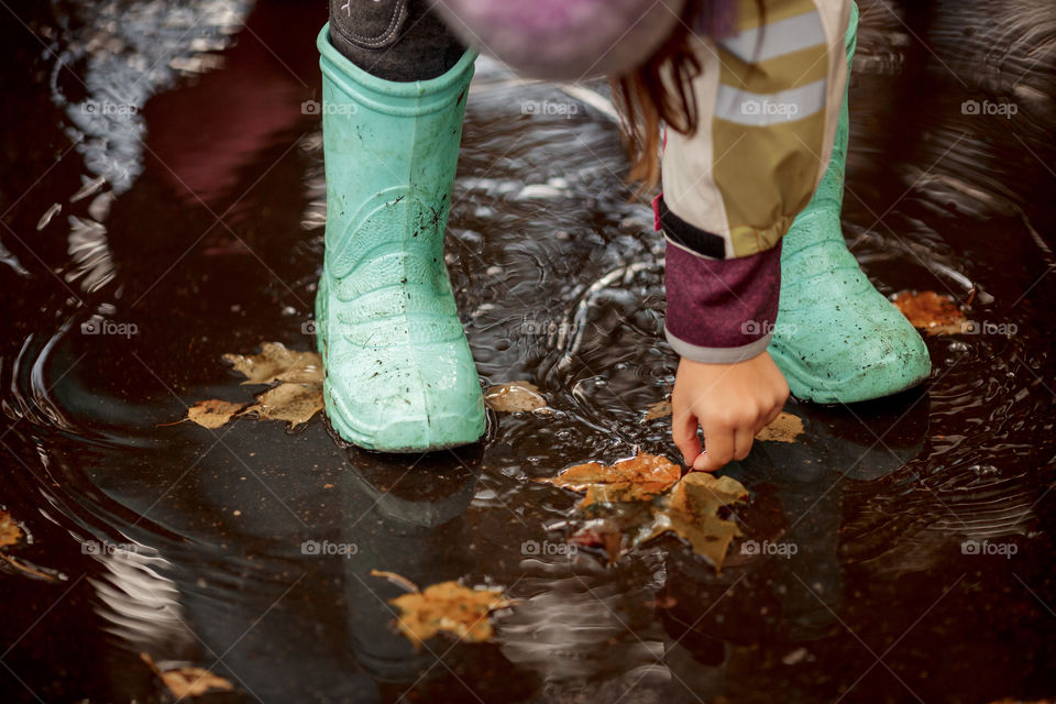 Little girl in rubber boots playing in puddle