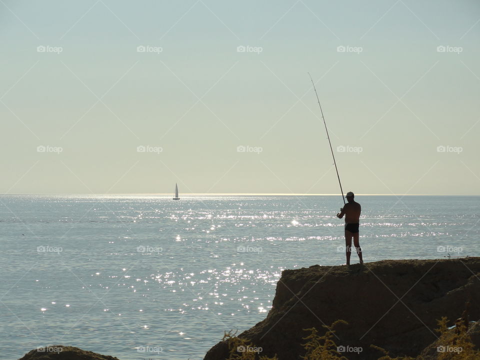 The fisherman and the ocean. just a guy fishing in the ocean on a big rock. he was just putting some new bait back on the hook of his fishing rod