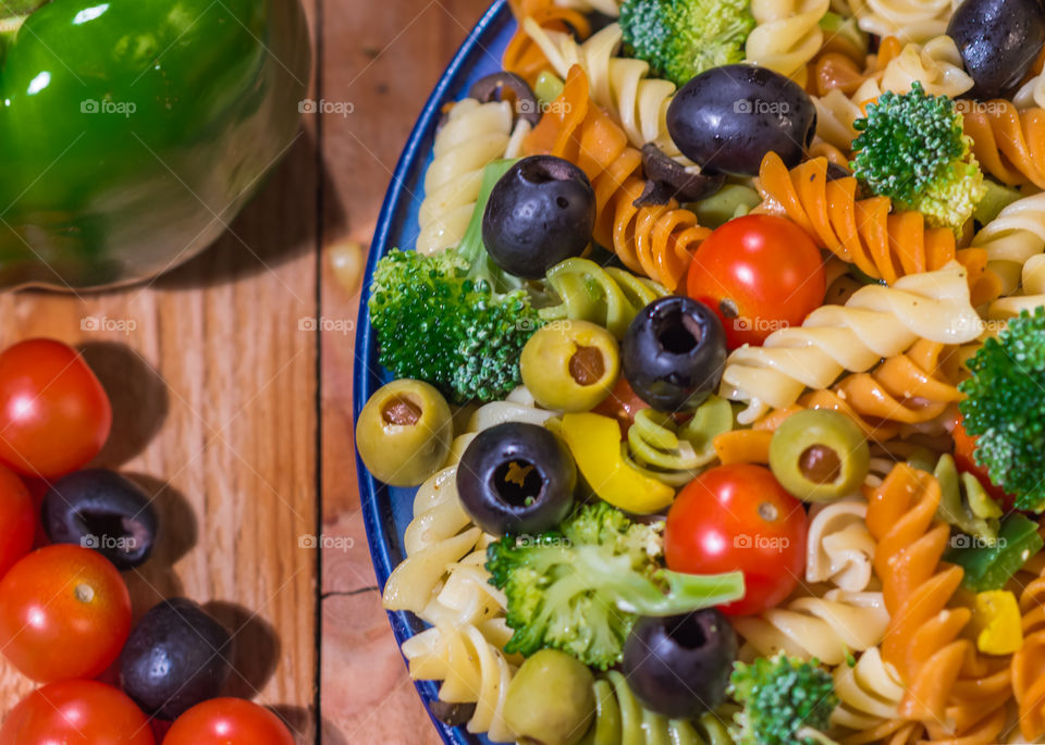 tri-color pasta salad with cherry tomatoes, broccoli, green peppers, black olives and green olives tossed with a light Italian dressing