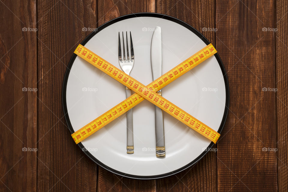 Fork and knife wrapped in measuring tape. Plate with a knife and fork wrapped in measuring tape on a wooden background. Healthy eating or dieting concept. Diet concept