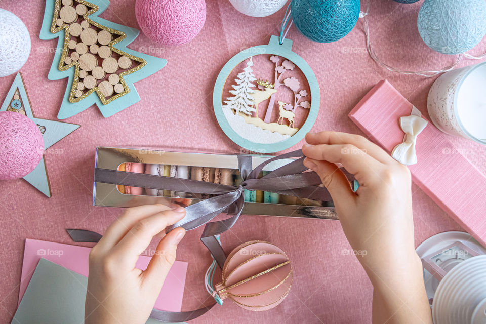 Hands of child make ribbon on the box with macarons. Perfect for Holidays. Decor on pink background.