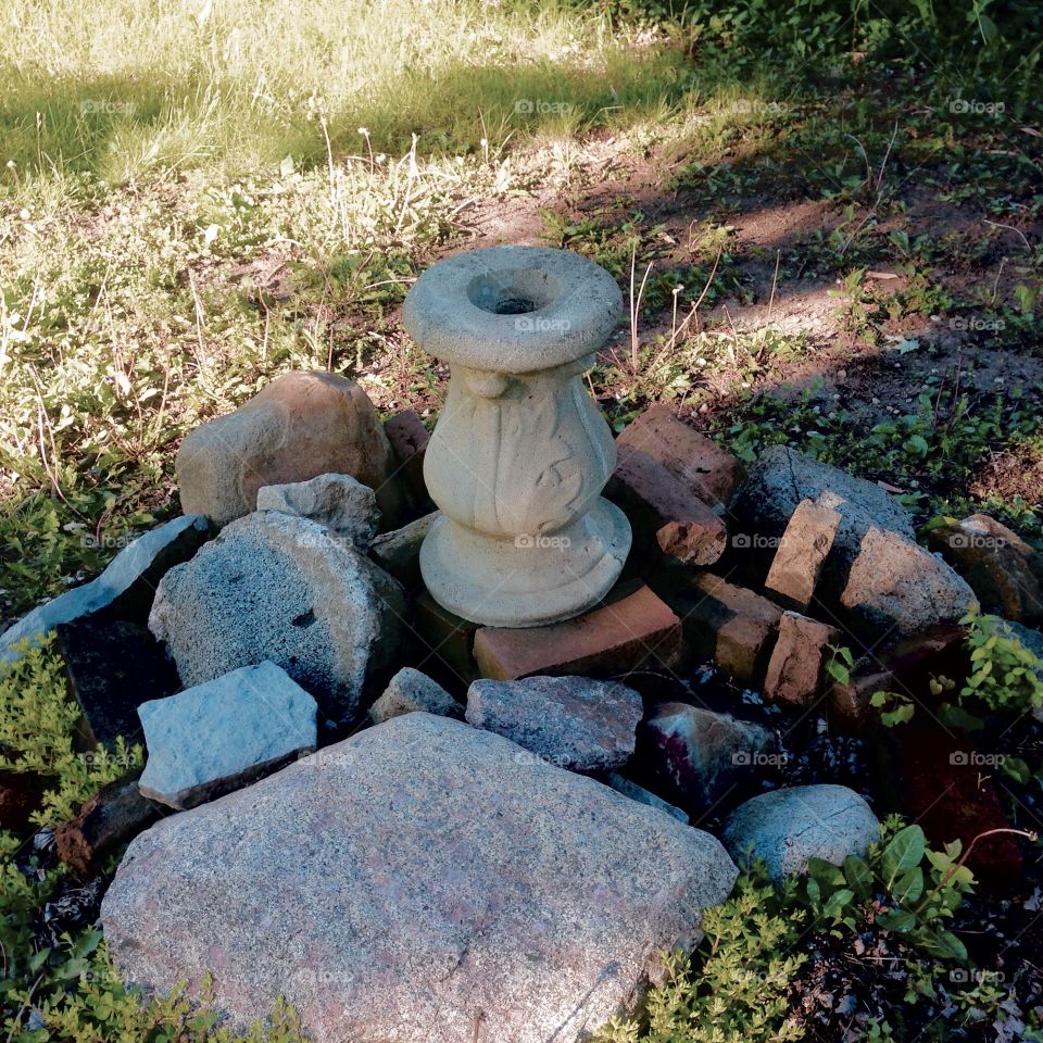 Sepia tones shot of broken bird bath sitting amongst discarded landscaping stones
