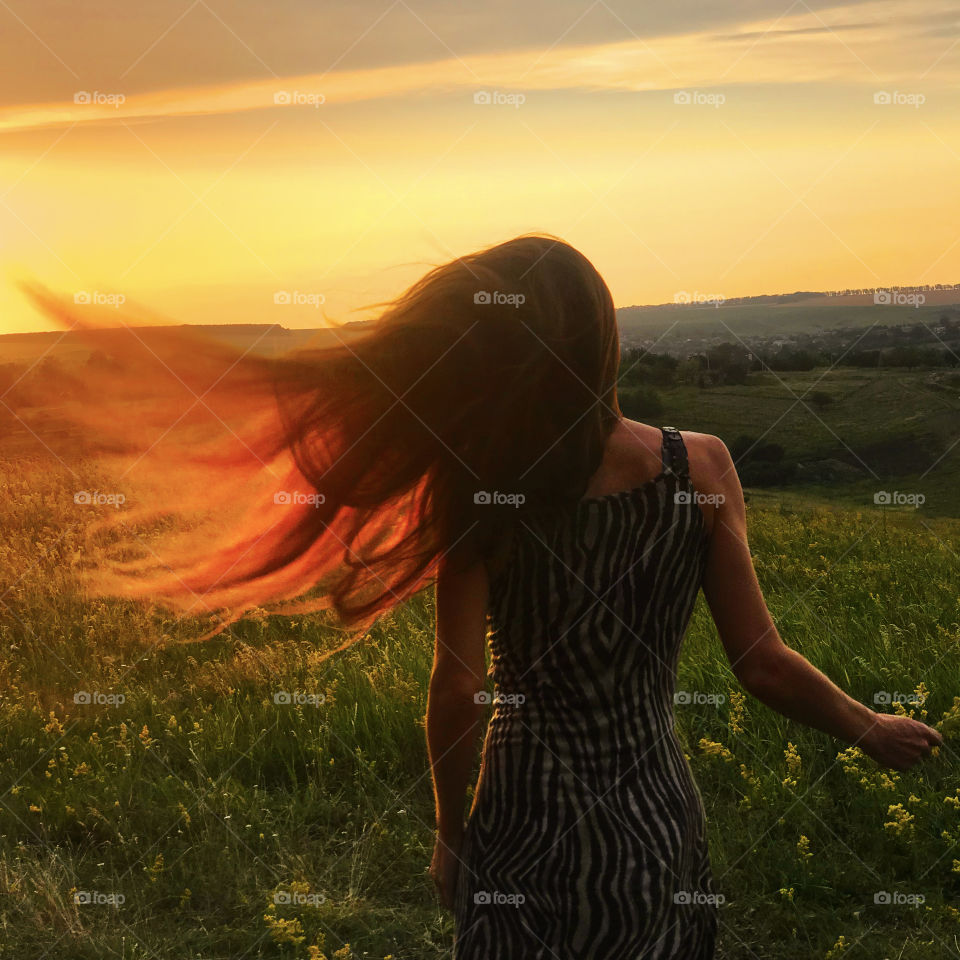 Young woman with long hair feeling freedom in the countryside flowering field during the sunset time 