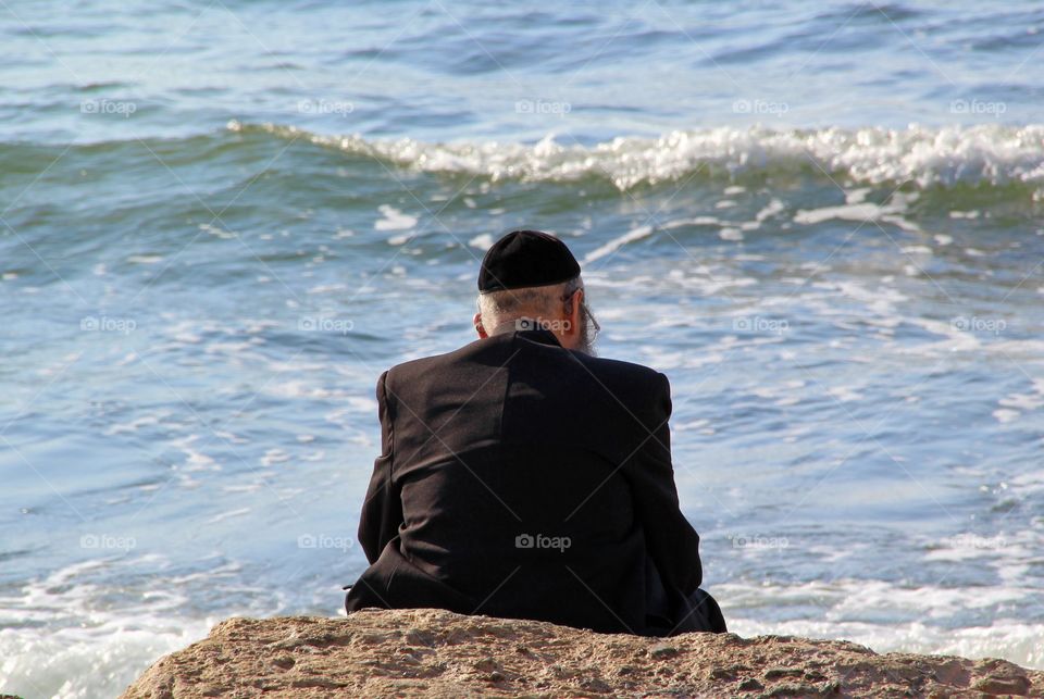 Religious Jew sitting on the coast of Mediterranean sea in Israel and watching the waves, deep in thought.