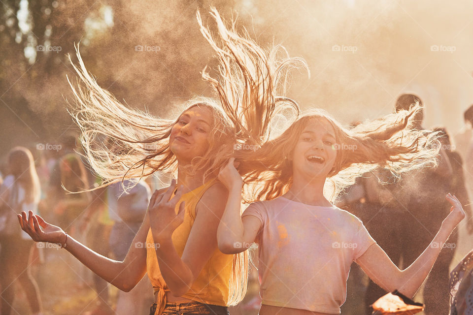 Portrait of happy smiling young girls with colorful paints on faces and clothes. Two friends spending time on holi color festival