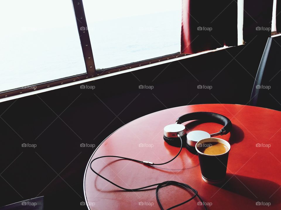 Coffee and headphones on a red table by the window