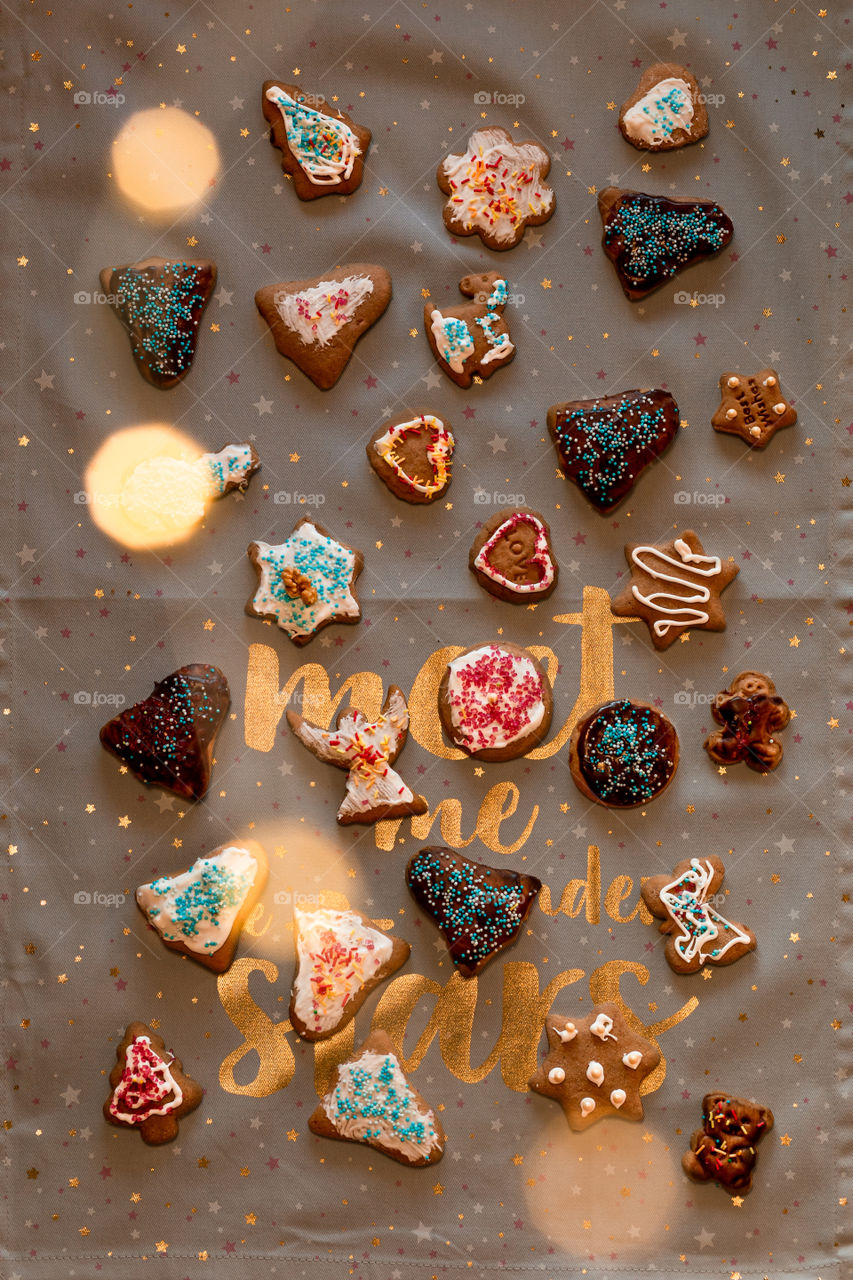 Christmas gingerbread cookies in many shapes decorated with colorful frosting, sprinkle, icing, chocolate coating, toppers, put on plain fabric