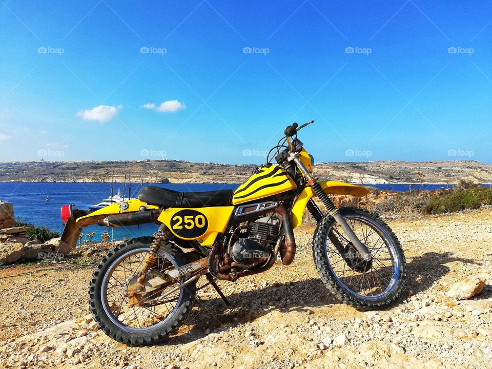 Yellow motocross bike in the foreground and background The wonderful sea of ​​the island of Comino