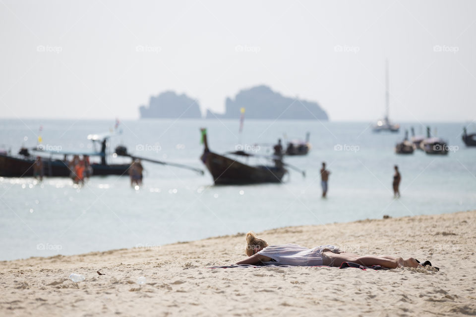 Female sunbathe in the sand of the beach with boat docking 