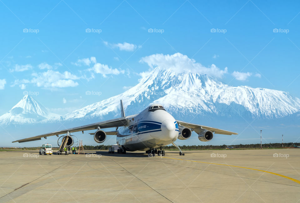 Maintenance of the world's largest transport aircraft Ruslan (Russia) at the airport of Yerevan (Armenia) against the background of very beautiful snow covered Ararat mountains, whose tops are buried in clouds, on a sunny spring day