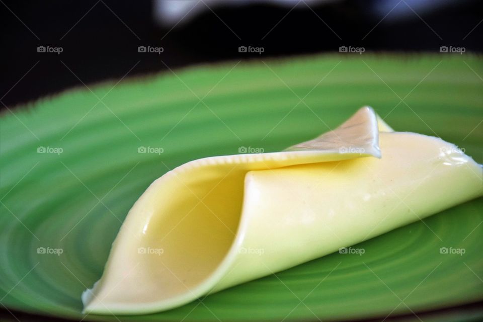 Slice of cheese on a green plate close up