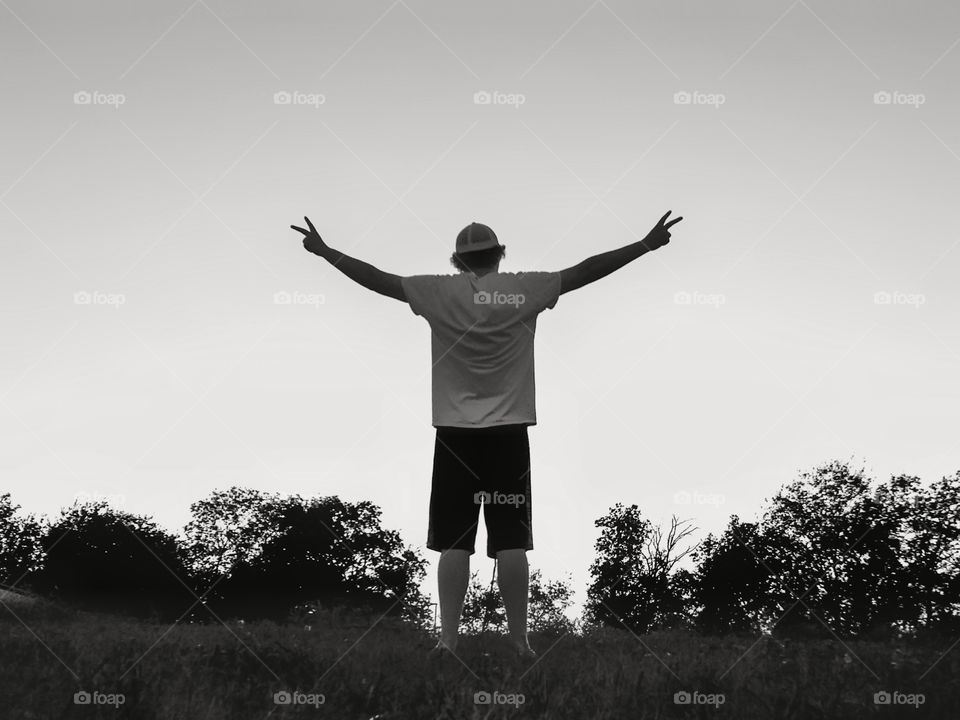 A man holding his hands up in the peace sign to the world in silhouette