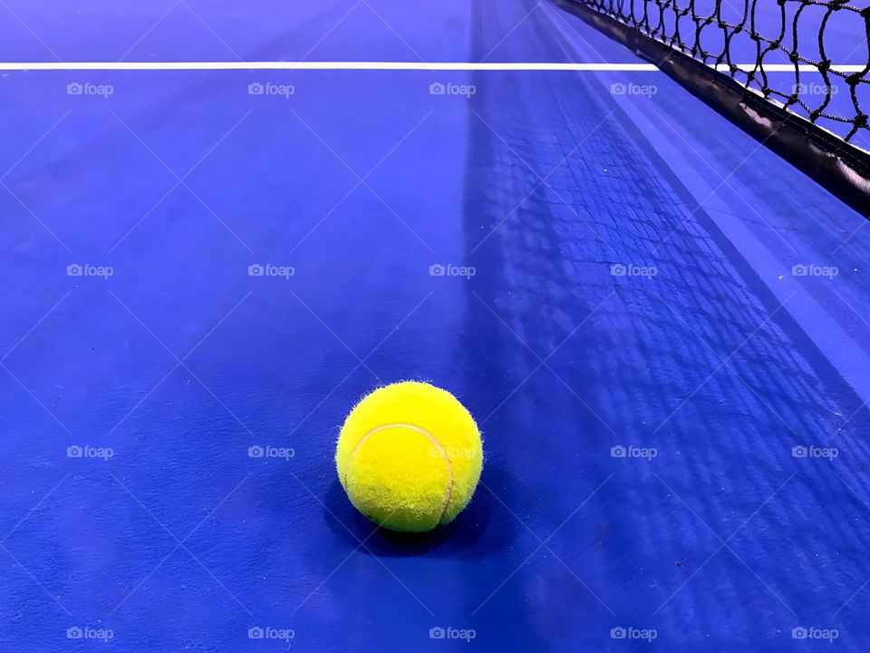 Yellow tennis ball on blue tennis court