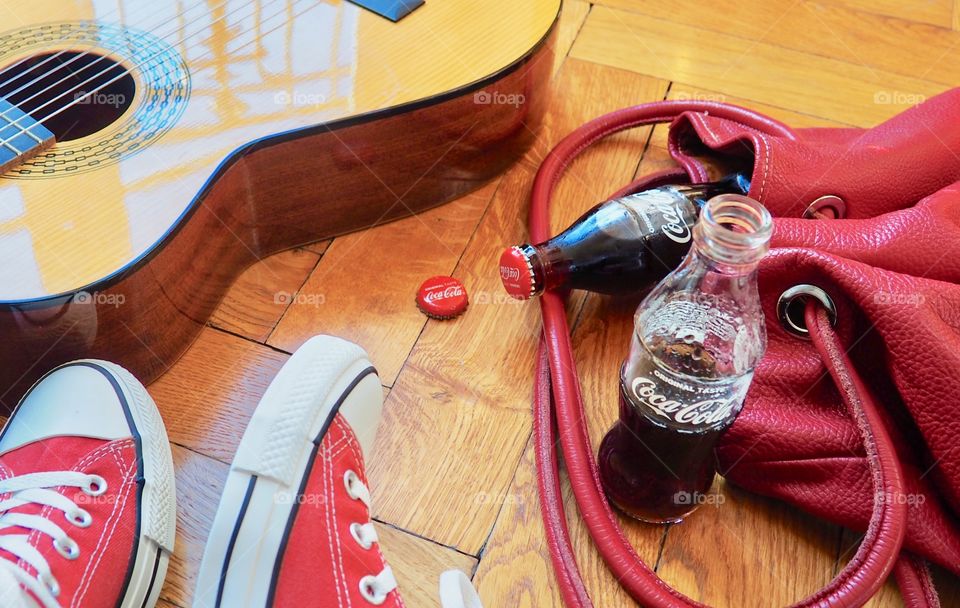 Coca Cola bottles on hardwood floor with red sneakers and red leather bag and guitar.