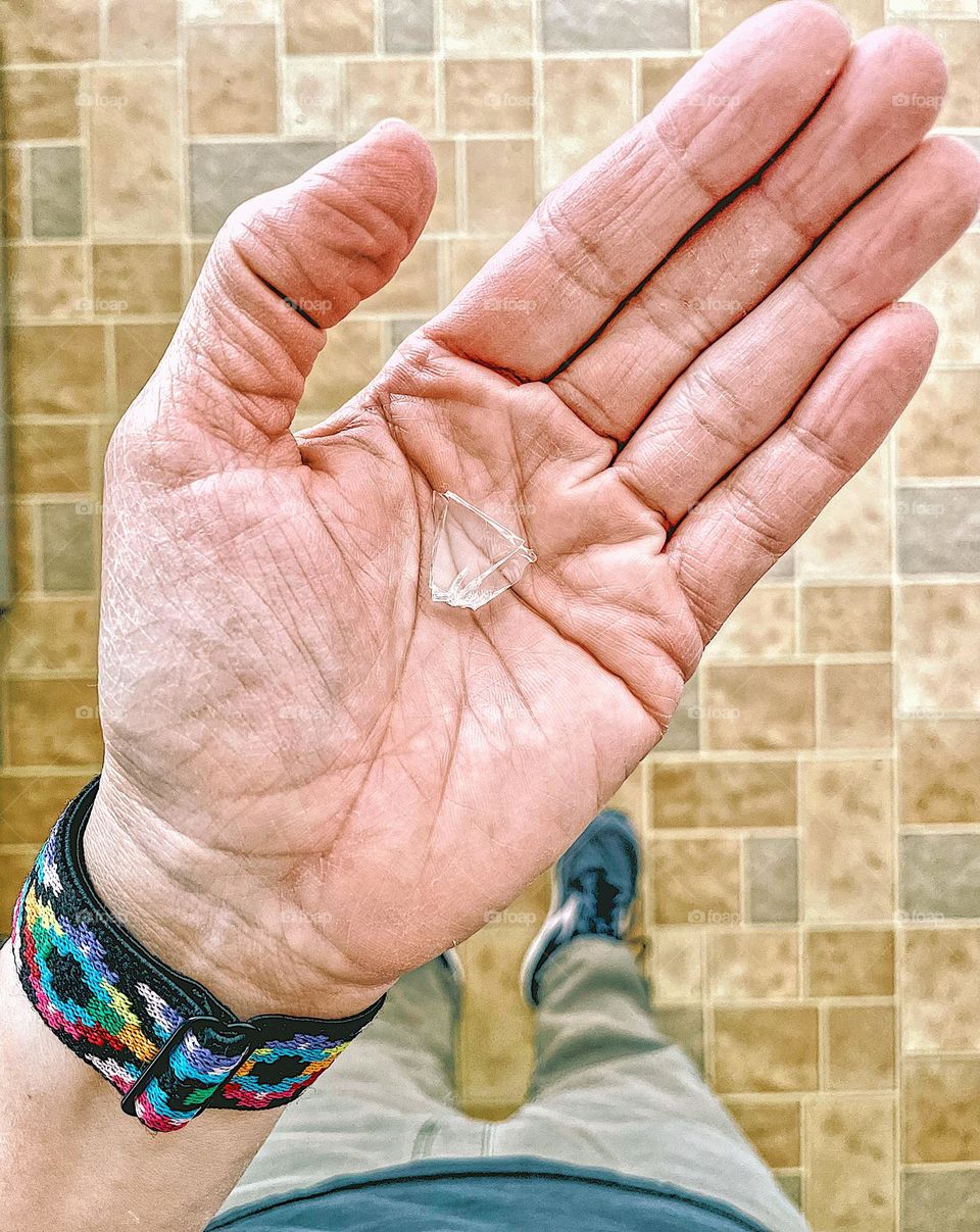 Woman’s hand holding a piece of broken glass, broken glass found on the floor, cleaning up broken glasses 