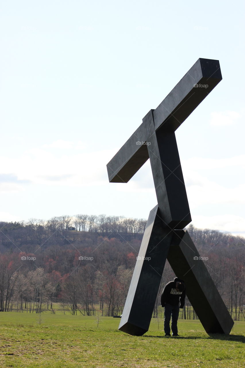 A man stands underneath one of the Storm King sculptures with the mountains behind him.