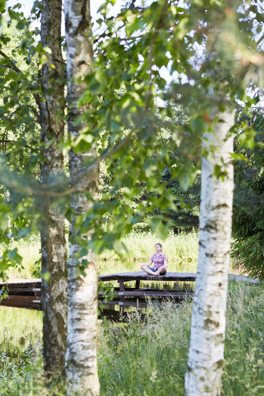 Woman sitting on a bridge over a lake, among the trees, close to nature, during summer vacations. Candid people, real moments, authentic situations