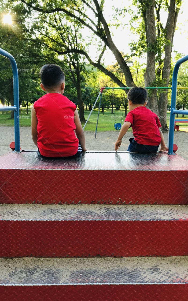 Two young boys in red going down a slide in a park