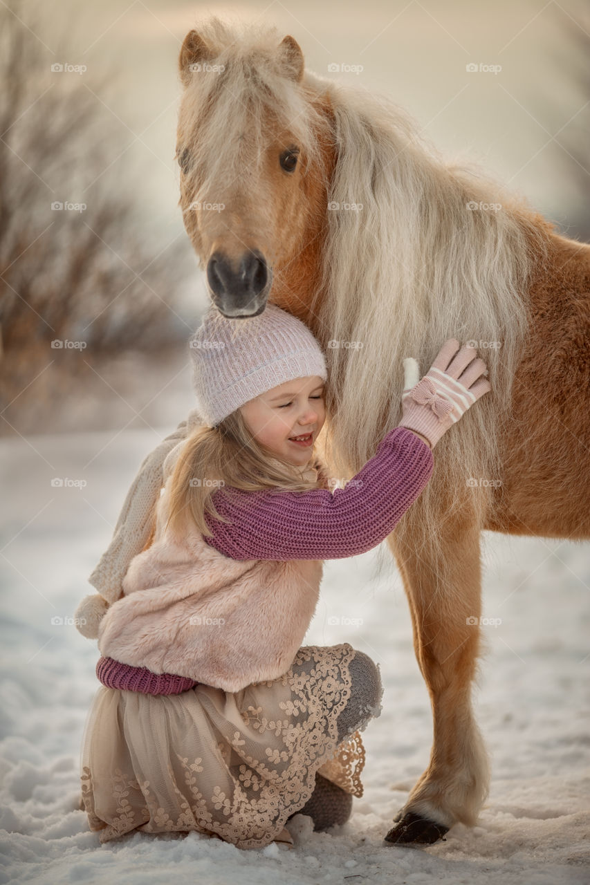 Little girl with pony at winter sunny day