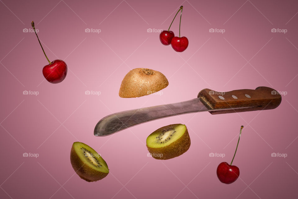 Old knife slicing kiwi fruit. Levitating food. Cherries falling down