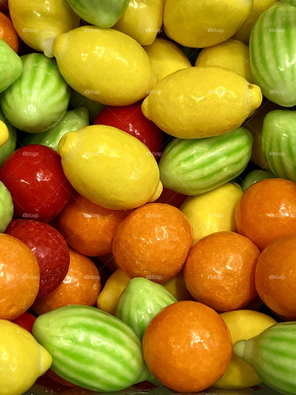 Bright fruit candies in the shape of lemons, oranges and other fruits lie on a white background. Juicy colors and detailed textures make them appetizing.