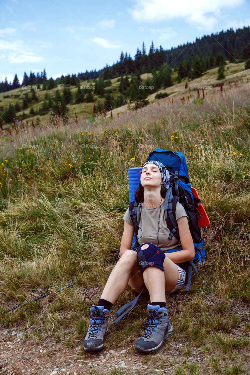 girl with a backpack sits in the wild nature, enjoys sounds and wind