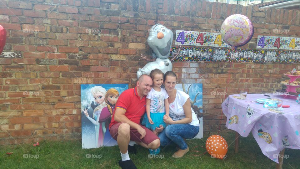 A little girl with father and mother posing against wall in her birthday