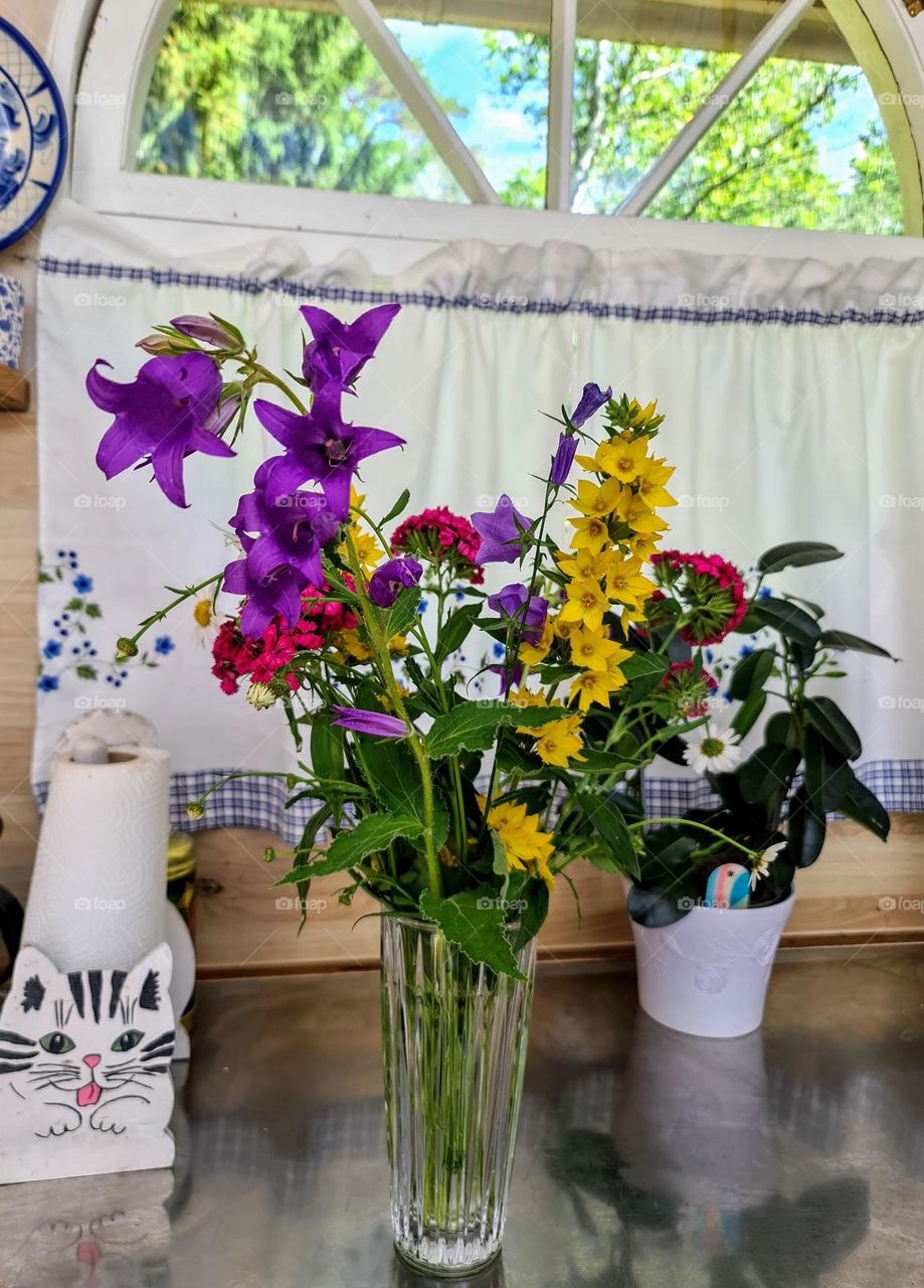 Close up of bright colorful summer flowers in the narrow transparent glass vase