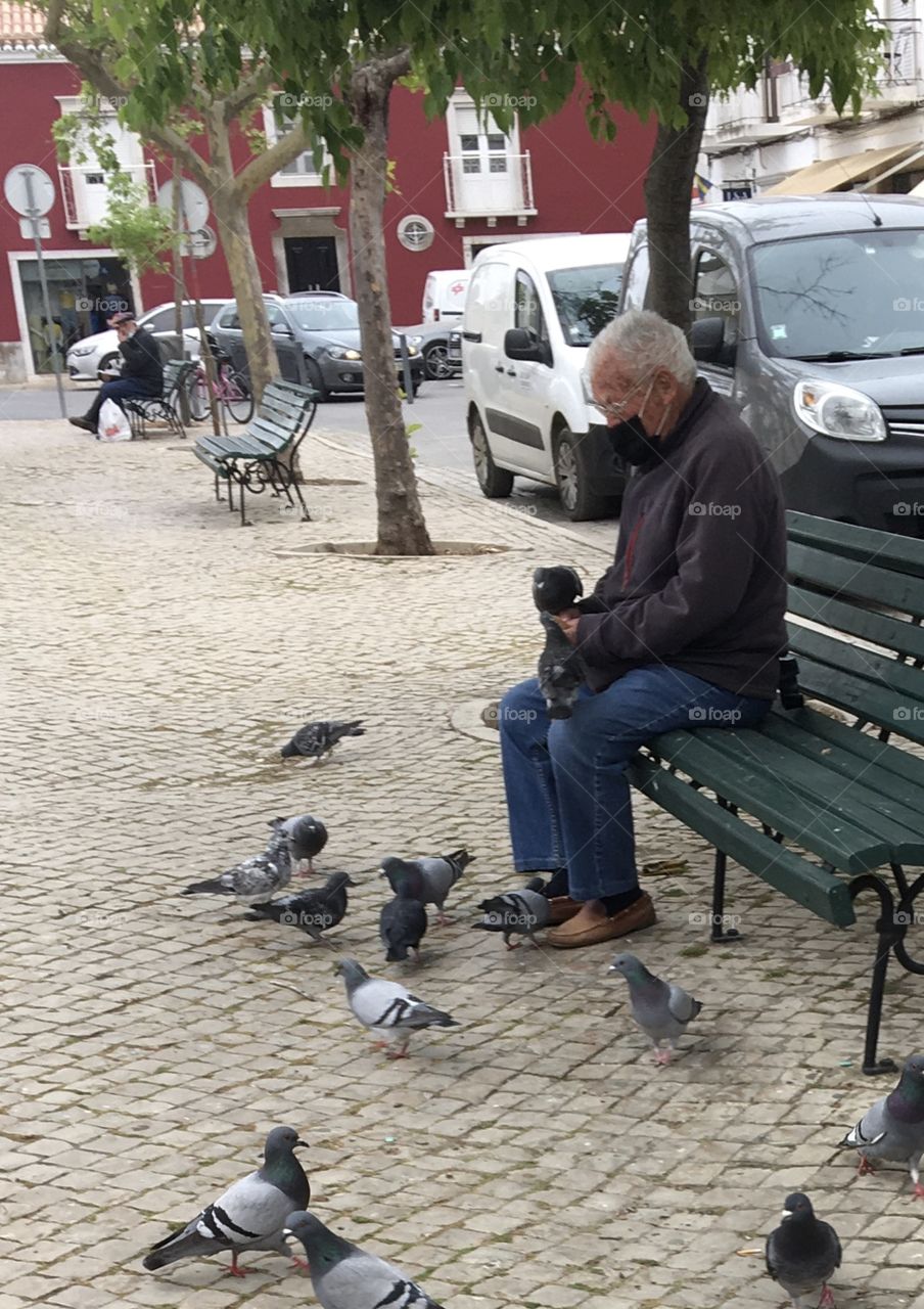 Old man with mask feeding and talking to doves 