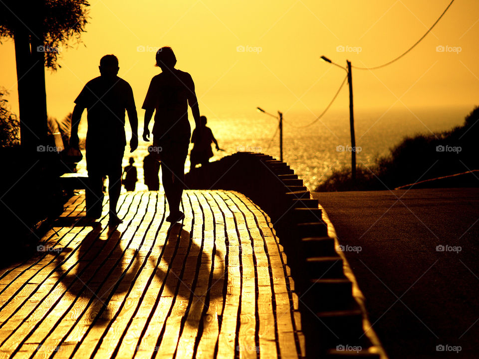 People walking on a beach wooden path while the sun sets