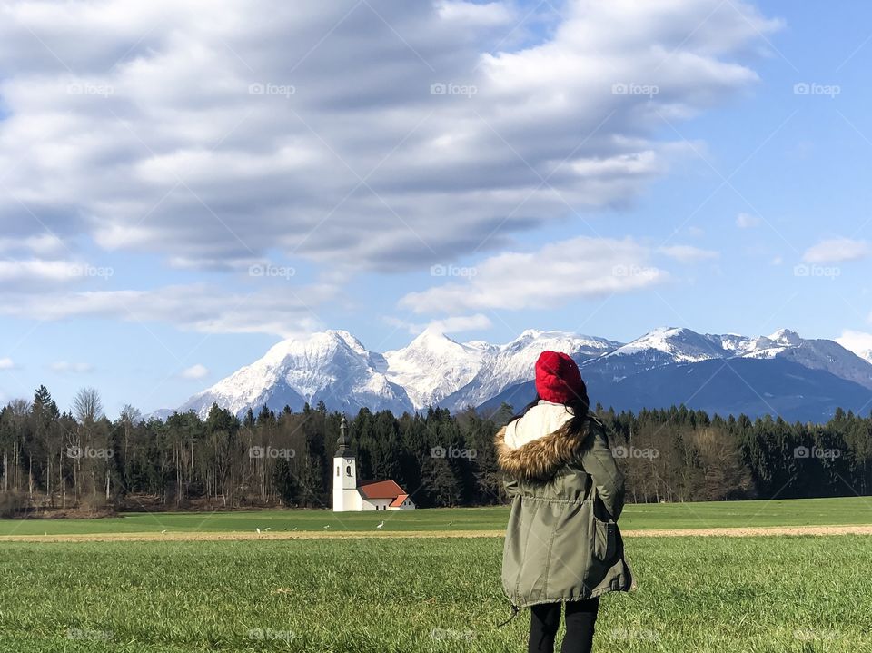 People from behind enjoying a sunny day in nature with view of church and snowy mountains on background 